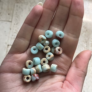 May include: A collection of light blue and brown speckled beads with a white bead in the center. The beads are round and have a hole in the center. They are perfect for making jewelry or other crafts.