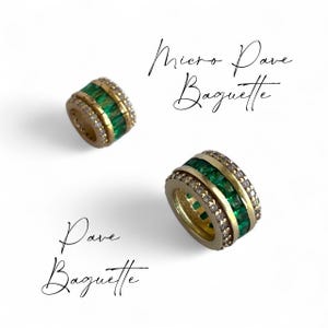 May include: Two gold rings featuring emerald-cut green gemstones and small clear stones. The rings are inscribed with "Micro Dave Baguette" and "Dave Baguette" in cursive. The rings are set against a white backdrop.