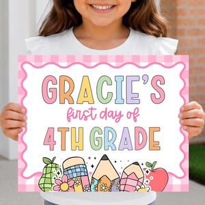 Könnte beinhalten: Ein rechteckiges Schild mit einem rosa karierten Rand und dem Text Gracie's first day of 4th Grade in bunten Buchstaben. Der untere Teil des Schildes ist mit Illustrationen einer Birne, Stiften und einem Apfel mit kleinen Blumen verziert.
