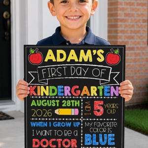 May include: A rectangular chalkboard sign for the first day of kindergarten featuring colorful text and graphics including apples, a pencil, and the name Adam. The sign displays details like the date August 28th 2026, age 5, career goal doctor, favorite color blue, and teacher Mrs. Jones.