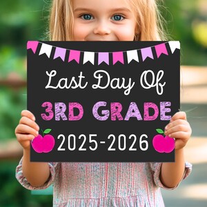 May include: A black chalkboard sign held by a child, with the text "Last Day Of 3RD GRADE 2025-2026" in white and pink. The sign is decorated with pink and white pennants and pink apple graphics.