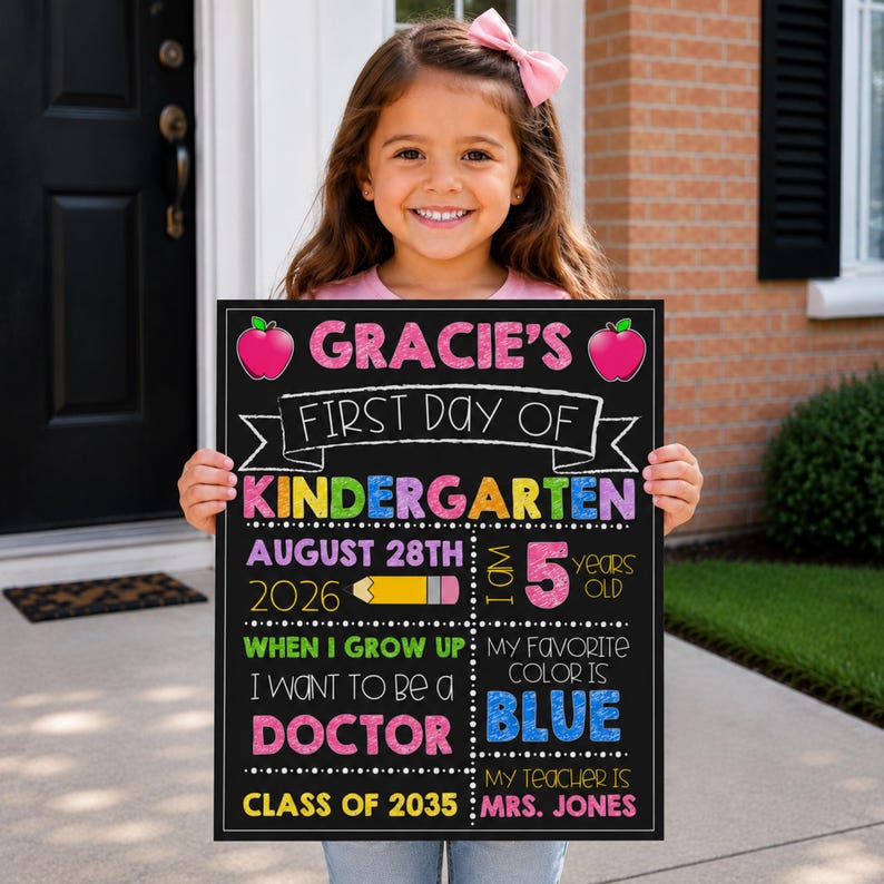 Op de afbeelding: Een rechthoekig krijtbord met een zwarte achtergrond en kleurrijke tekst. Er staat op: Gracie's First Day of Kindergarten, August 28th 2026, I am 5 years old, When I grow up I want to be a doctor, My favorite color is blue, Class of 2035, Mrs. Jones.