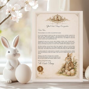 Puede incluir: Una figura de conejito de Pascua de cerámica blanca con orejas largas y un acabado liso, junto a un huevo blanco. También hay una carta decorativa con el texto "Official Easter Bunny Correspondence" y una ilustración de acuarela de un conejo.