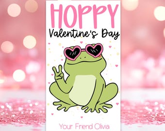 Peut inclure: Une carte de Saint-Valentin avec une grenouille verte portant des lunettes de soleil en forme de cœur rose et faisant un signe de paix. La carte dit "Hoppy Valentine's Day" et "Your Friend Olivia".