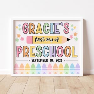 以下が含まれることがあります： カラフルな文字で「Gracie's first day of Preschool」と書かれた額入りのプリント。中央には黄色の鉛筆のグラフィックがあり、その下に日付「September 10, 2026」があります。パステルカラーのクレヨンが下部を飾っています。