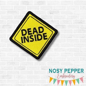 May include: A yellow embroidered patch with the words "DEAD INSIDE" in black, inside a black-bordered yellow diamond. The patch is part of the "AUGUST 2025 MEGA BUNDLE" collection.