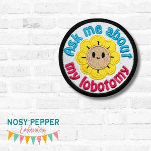 May include: Embroidered patch with a smiling sunflower design. The patch has the text "Ask me about my lobotomy" in a circular pattern around the flower. The patch is black, white, yellow, pink, and blue. The text "July 2025 mega Bundle" is above the patch.