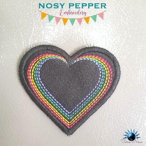 Op de afbeelding: Een zwarte hartvormige patch met een regenboog geborduurd rond de rand. De regenboog is gemaakt van rood, oranje, geel, groen, blauw, indigo en violet.
