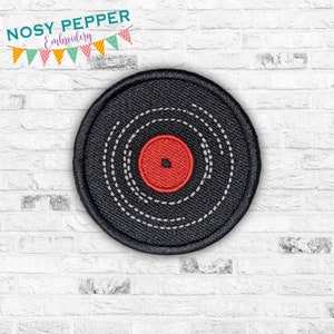 May include: A black and white embroidered vinyl record patch with a red center. The patch is circular and has a stitched edge.