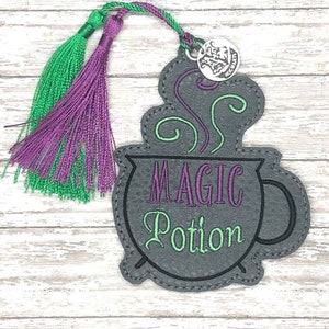 May include: A grey felt bookmark with a cauldron and the text "MAGIC Potion" in purple and green embroidery. The bookmark has a green and purple tassel.