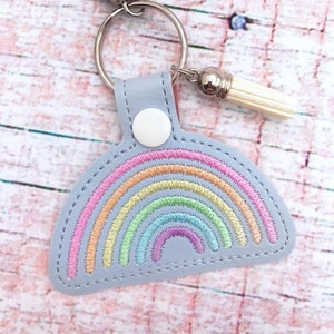 May include: A light blue leather keychain with a rainbow embroidered design and a silver charm with a white tassel.