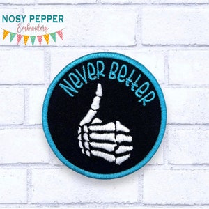 Puede incluir: Un parche bordado en blanco y negro con una mano de esqueleto haciendo un pulgar hacia arriba. El parche está rodeado por un borde turquesa y las palabras "Never Better" están bordadas en blanco alrededor de la mano.