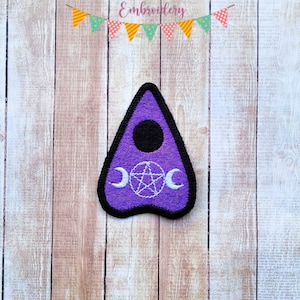 May include: Purple felt patch with a white pentagram and crescent moons, resembling a Ouija board planchette.