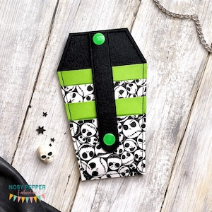 Puede incluir: Una funda para teléfono con forma de ataúd con la parte superior y la correa negras, detalles en verde y un estampado de caras de Jack Skellington. La funda tiene dos cierres de botón a presión verdes.