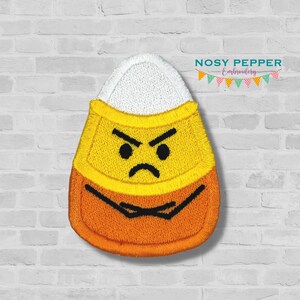 May include: An embroidered iron-on patch of a candy corn with an angry face. The candy corn is yellow, orange, and white. The patch is perfect for adding a fun and festive touch to your Halloween crafts.
