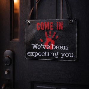 May include: Black rectangular sign with the text "COME IN" in red, a red handprint, and the text "We've been expecting you" in white. The sign is hanging on a black door.
