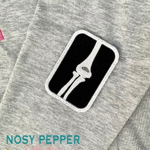 Puede incluir: Una sudadera gris con un parche bordado en blanco y negro de una imagen de rayos X de un codo.