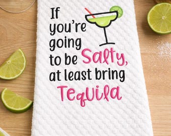 May include: White kitchen towel with a textured pattern, embroidered with the phrase "If you're going to be Salty, at least bring Tequila." A lime margarita graphic is also included. Limes and salt are in the background.