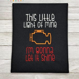 May include: Black fabric with white embroidery that reads "This little light of mine I'm gonna let it shine" with a yellow check engine light graphic.