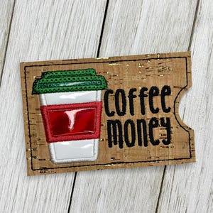May include: A cork coffee sleeve with a stitched design of a coffee cup and the words "coffee money" in black. The coffee cup has a green lid, a red band, and a white cup.