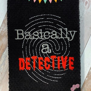 May include: Black kitchen towel with white embroidery of a fingerprint and the text "Basically a Detective".