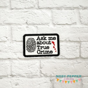 以下が含まれることがあります： 指紋と「Ask me about True Crime」というテキストが刺繍された白黒のパッチ。テキストは黒で、テキストの隣には赤い血しぶきがあります。