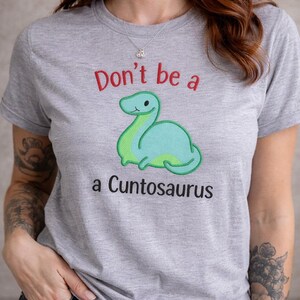 Könnte beinhalten: Eine weiße Keramik-Tasse mit schwarzem Henkel und dem Text "But First, Coffee" in fetter, schwarzer Schrift. Die Tasse steht vor einem verschwommenen Hintergrund, der eine gemütliche Umgebung andeutet.