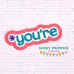 Może przedstawiać: Haftowany naszywka w kolorze różowym i białym z tekstem "*you're" w turkusowych literach. Naszywka znajduje się na białym tle z cegły.
