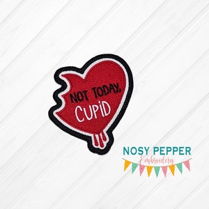 Puede incluir: Un parche rojo en forma de corazón con un contorno negro y costuras blancas. El corazón está roto y dice "Not Today, Cupid" en texto blanco.