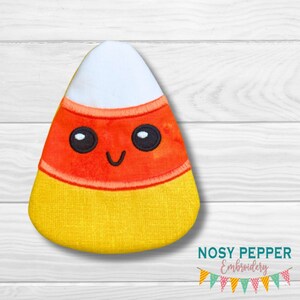 Puede incluir: Un juguete de peluche con forma de maíz dulce con una cara sonriente y ojos negros. El maíz dulce es amarillo, naranja y blanco.