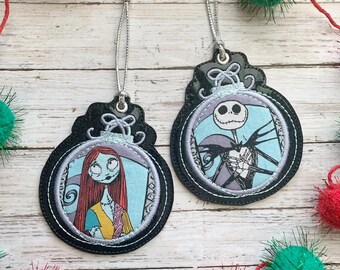 May include: Two black and silver Christmas ornaments with embroidered images of Jack Skellington and Sally from the Nightmare Before Christmas movie. The ornaments are hanging from silver cords.