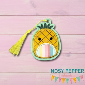 Puede incluir: Un marcapáginas amarillo con forma de piña con una cara sonriente y una barriga de colores arcoíris. El marcapáginas tiene un borde verde y una borla amarilla. El texto "NOSY PEPPER Embroidery" está en la parte inferior.