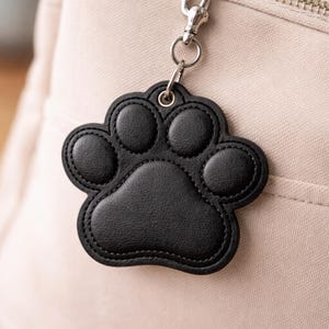 May include: Black paw print keyring with a silver clasp, attached to a light-coloured bag. The paw print is made of stitched black material. The text "NOSY PEPPER Embroidery" is visible at the bottom of the image.