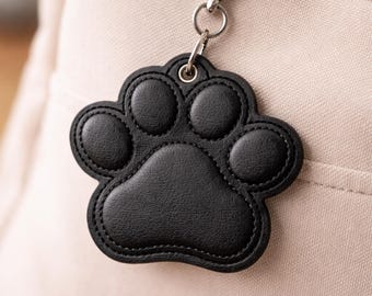 May include: Black paw print keychain with a silver clasp, attached to a light-colored bag. The paw print is made of stitched black material. The text "NOSY PEPPER Embroidery" is visible at the bottom of the image.