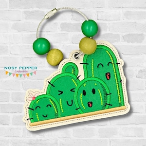 May include: A green cactus keychain with a smiling face and a small cactus with a smiling face. The keychain has a metal ring and wooden beads.