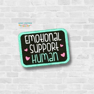 Op de afbeelding: Een geborduurde zwarte en witte patch met een turquoise rand. De patch zegt "Emotional Support Human" met roze harten.