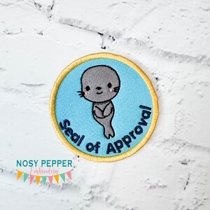 May include: A round blue and yellow embroidered patch with a cartoon seal and the text "Seal of Approval".