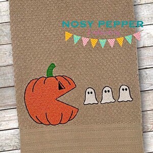May include: An orange pumpkin with a Pac-Man mouth is chasing three white ghosts. The pumpkin has a green stem. The ghosts have black eyes. The background is a brown fabric with a banner of colorful triangles.