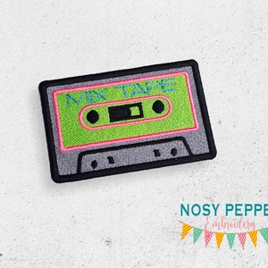 Puede incluir: Un parche bordado de una cinta de casete gris y negro, con el texto "MIX TAPE" en letras verdes, rosas y azules.