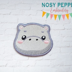 May include: Embroidered iron-on patch of a gray hippopotamus face with pink cheeks and black eyes. The patch is on a white brick background. The text "NOSY PEPPER Embroidery" is at the top of the image.