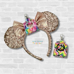 May include: Rose gold sequined mouse ear headband with a matching bow and a geometric design keychain. A second keychain with a colorful, wavy pattern is also included. The text "NOSY PEPPER Embroidery" is visible.
