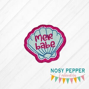 May include: A pink and blue embroidered patch with a seashell design and the text "mer babe".