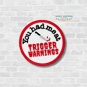 Może przedstawiać: Naszywka haftowana na czerwono i biało z tekstem "You had me at trigger warnings" i grafiką noża.