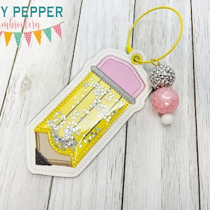 May include: A yellow pencil-shaped bookmark with a pink eraser and silver glitter inside. The bookmark has a yellow loop and is adorned with decorative beads. The top left corner of the image has the text "NOSY PEPPER Embroidery".