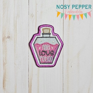 Puede incluir: Parche bordado de color morado con forma de frasco de poción con un tapón de corcho. El frasco contiene líquido rosa y purpurina. El texto en el frasco dice "Anti Love Potion".