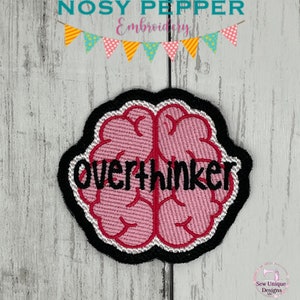 Op de afbeelding: Een roze geborduurd brein met een zwarte omtrek en het woord "overthinker" in zwarte tekst.