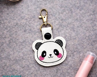 May include: A white panda bear keychain with black and pink accents. The keychain has a gold-colored clasp and a black button detail. The design is on a white leather-like material. The brand name "NOSY PEPPER" is at the bottom.