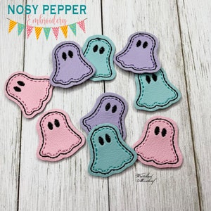 May include: Nine felt ghost shapes in various colors, including pink, purple, and blue, with black embroidered eyes. The ghosts are arranged in a circle on a light wood background.