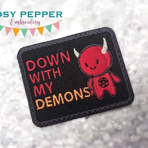 May include: Black embroidered patch with the text "Down with my demons" in red and orange thread. A red cartoon devil with white horns and a pentagram on its chest is to the right of the text.