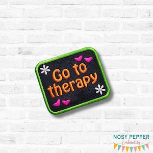 May include: Embroidered patch with the words "Go to therapy" in orange, surrounded by pink hearts, white flowers, and a green border. The patch is on a black background.